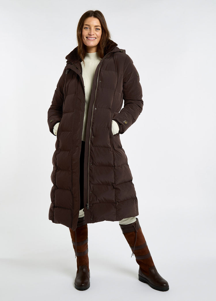 Woman wearing a mahogany full length down jacket with hood over a cream sweater and brown riding boots