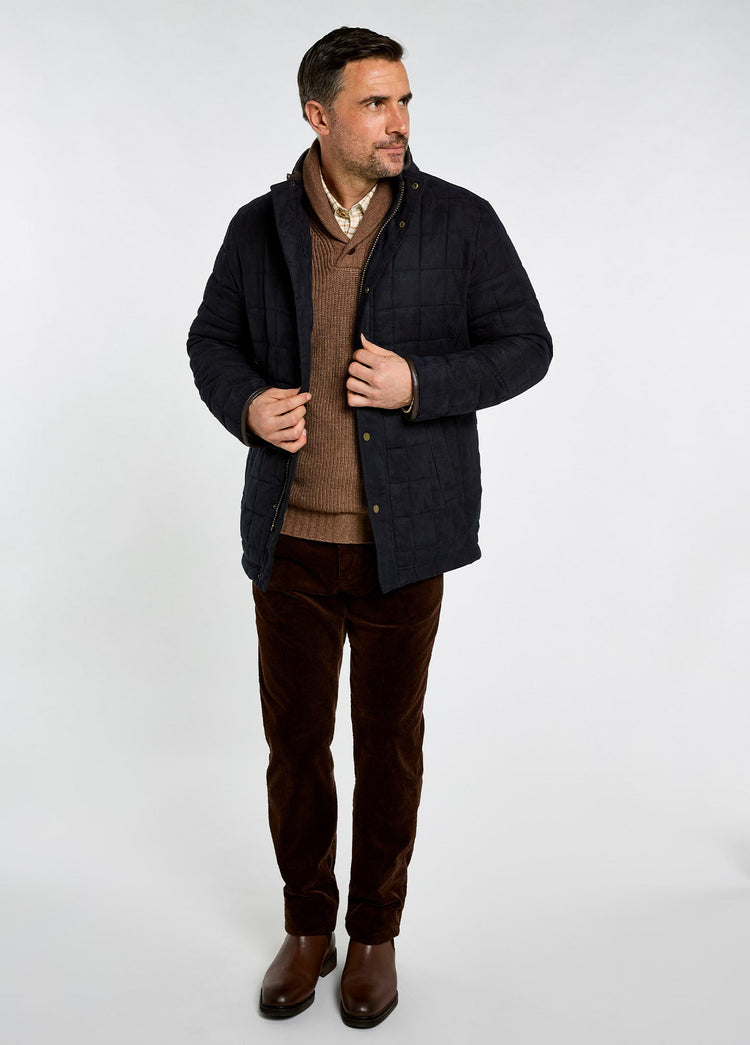Man wearing a navy quilted jacket with subtle herringbone texture over a brown sweater and trousers