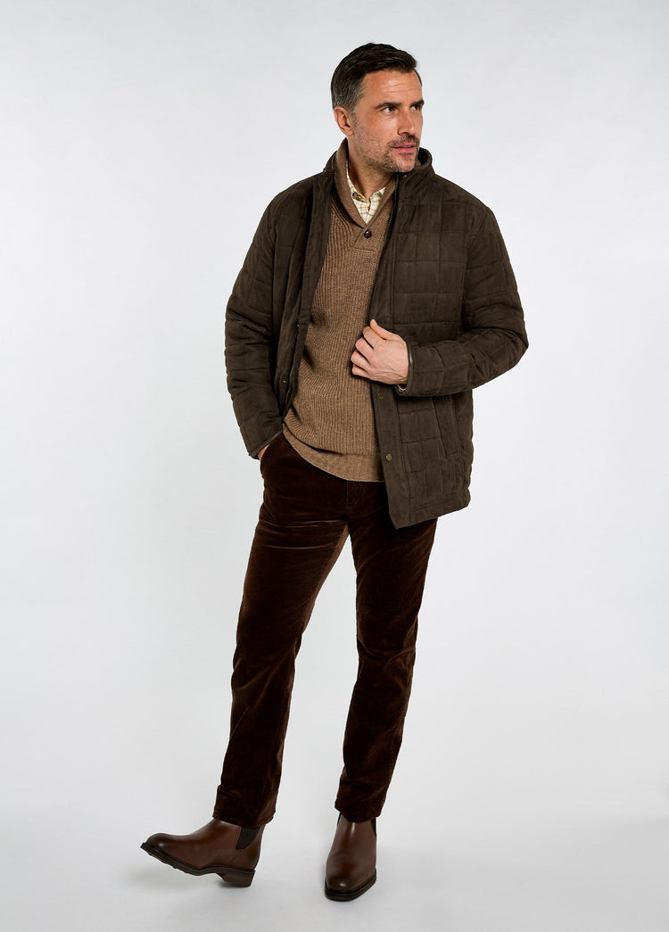Man wearing an olive quilted jacket with a brown sweater, dark trousers and leather boots for a refined country clothing look