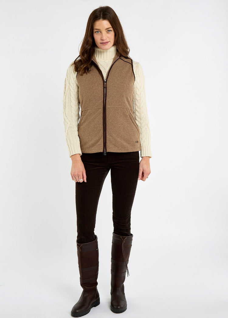 Woman wearing an elk fleece vest over a cream cable knit sweater with dark trousers and tall brown riding boots for country wear