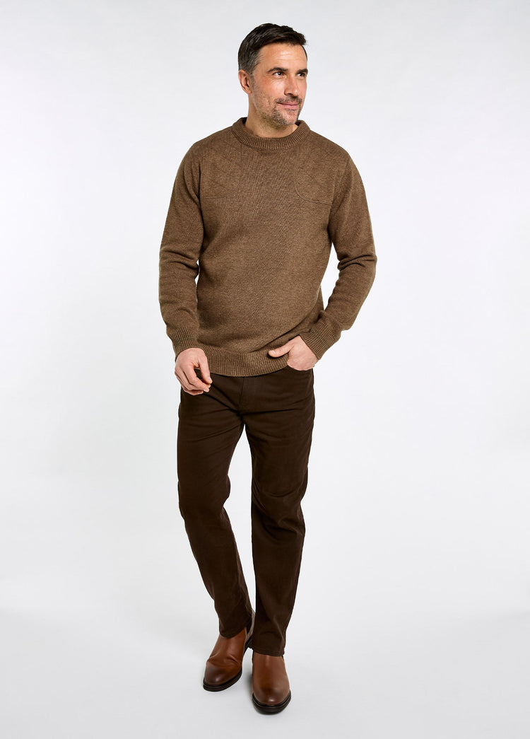 Man wearing an Elk crew neck wool blend sweater with dark trousers and brown leather shoes in a studio setting