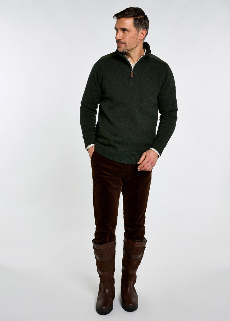 Man wearing an olive wool blend zip neck sweater with brown trousers and tall leather country boots posing against a light background