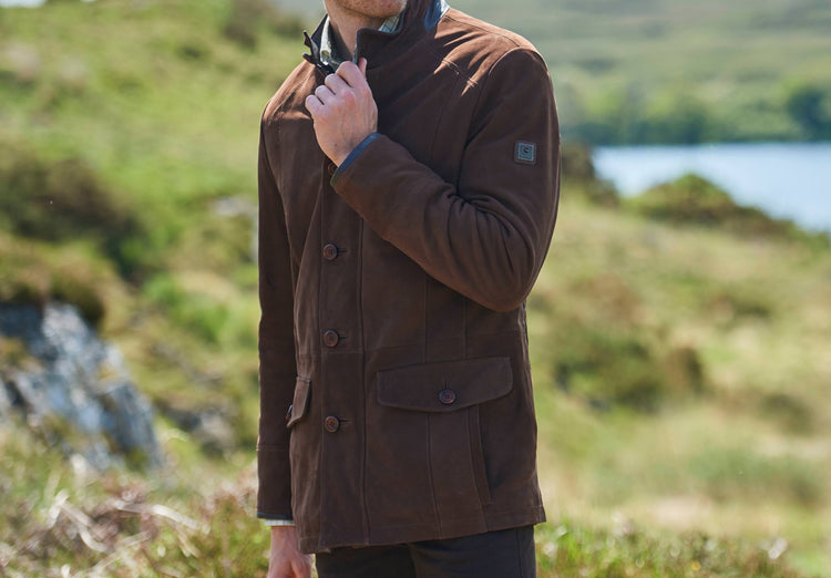 Man wearing a walnut leather country jacket with stand collar, button front and flap pockets in a scenic rural setting