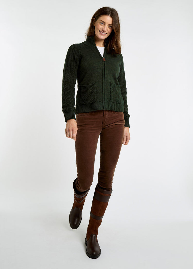 Woman wearing an olive full zip knit sweater with brown trousers and tall brown leather country boots