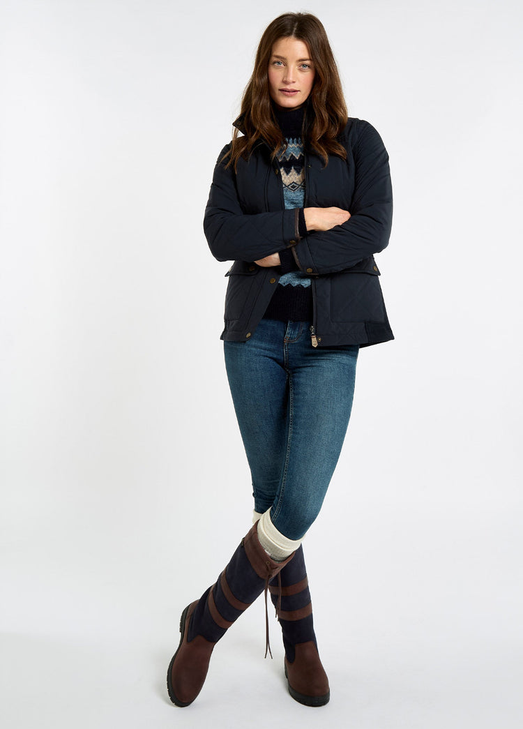 Woman wearing a navy lightweight jacket with knit side panels, jeans and brown leather country boots against a light background