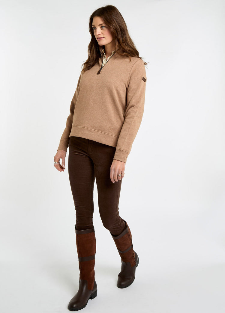 Woman wearing an Elk quarter zip sweatshirt with dark trousers and brown leather riding boots in a studio setting