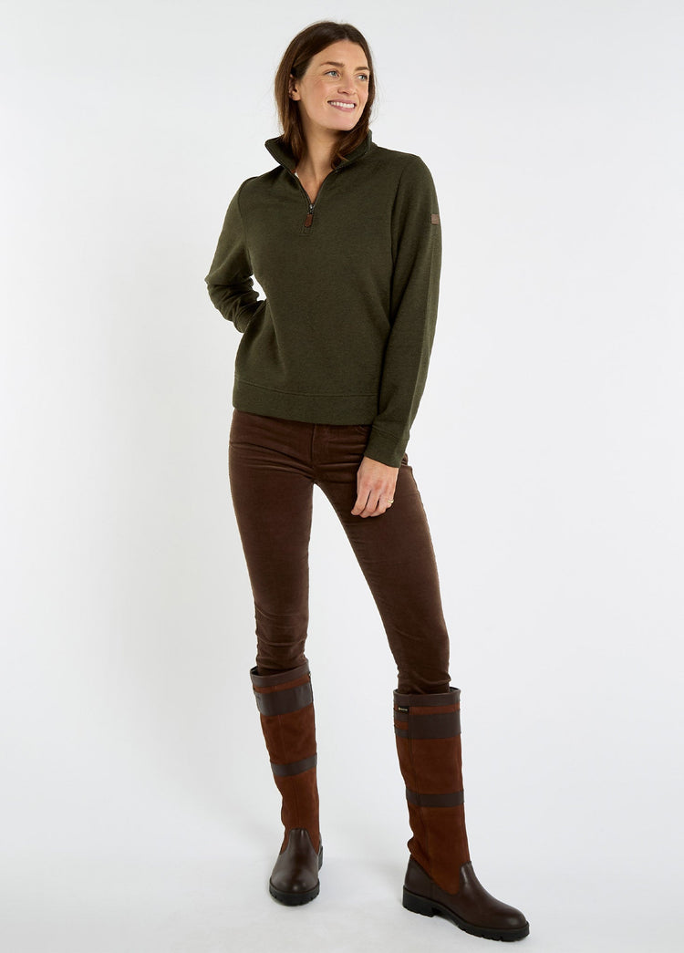 Woman wearing an olive quarter zip sweatshirt with brown trousers and tall leather country boots in a relaxed outdoor clothing style